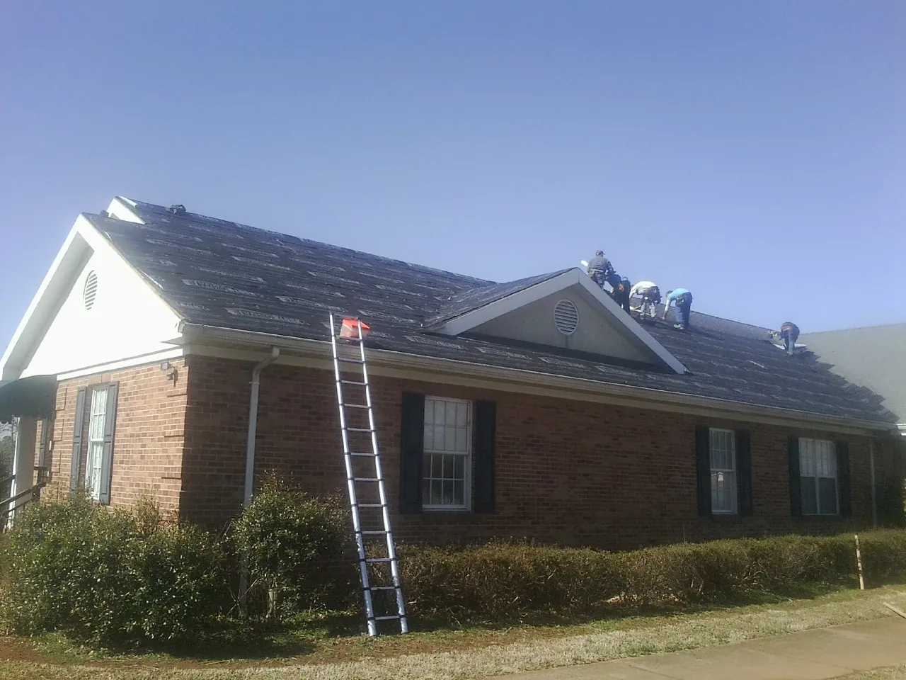Crew tearing shingles off a brick ranch roof with a ladder set — Emergency Roof Repair work by our crew in Red Oak